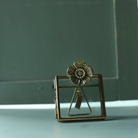 Decorative brass flower-shaped object on a light surface with a green background